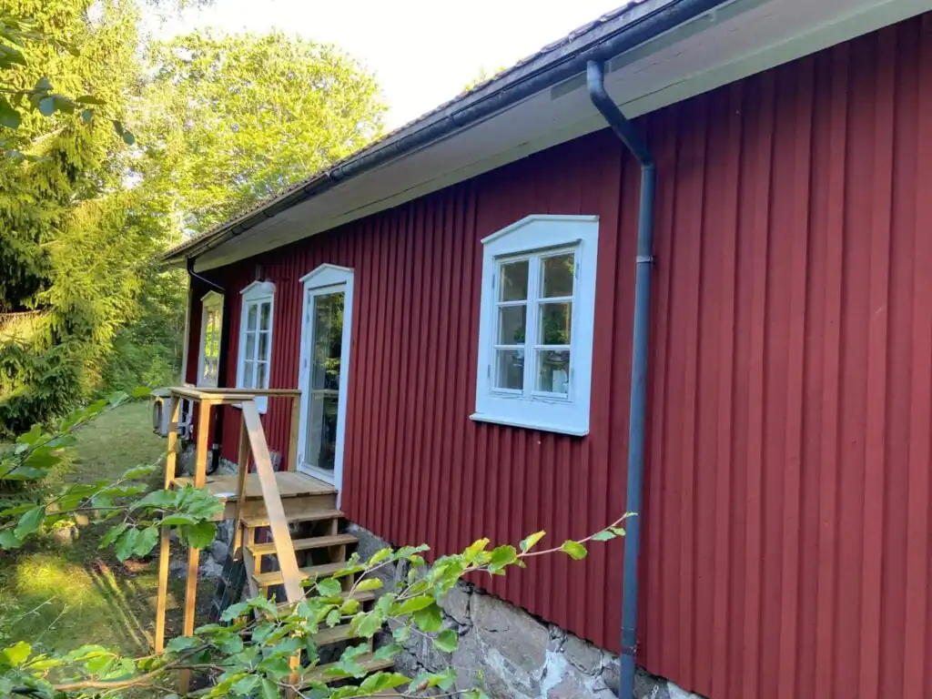 Detailansicht der roten Holzfassade des Ferienhauses Torsholma Skolhus mit weißen Fenstern im traditionellen Schwedensti